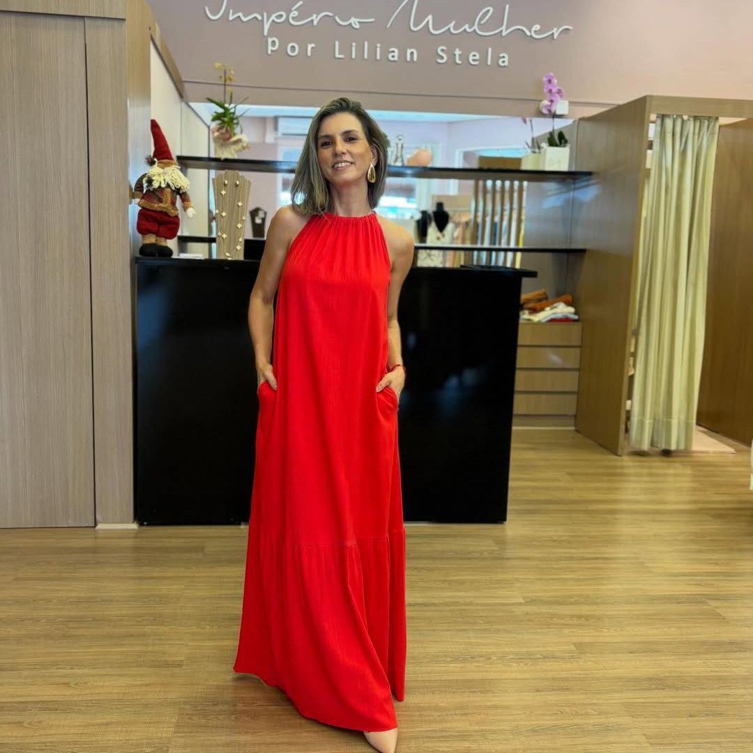 Modelo vestindo vestido longo vermelho, com gola alta, modelagem ampla. recorte na saia e bolsos laterais.