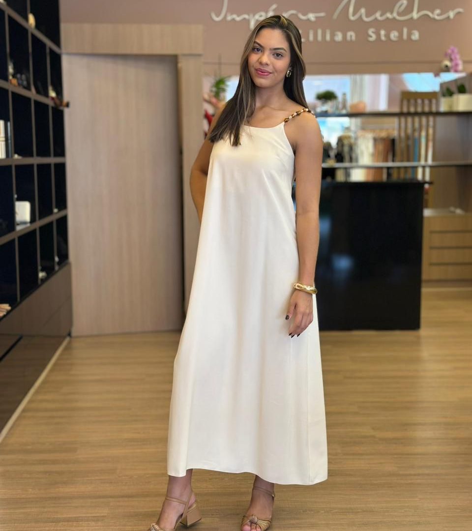 Modelo vestindo vestido midi off-white de alças finas com detalhe em corrente.