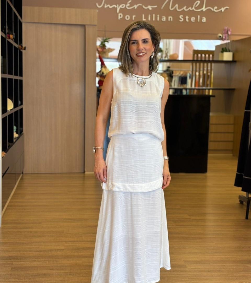 Modelo veste conjunto branco composto por blusa sem mangas e saia longa, em tecido leve e fluido.