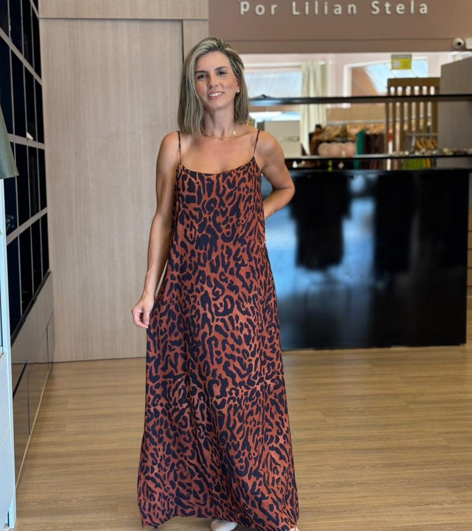 Vestido longo marrom com estampa animal print preta, alças finas e modelagem solta, usado com salto.
