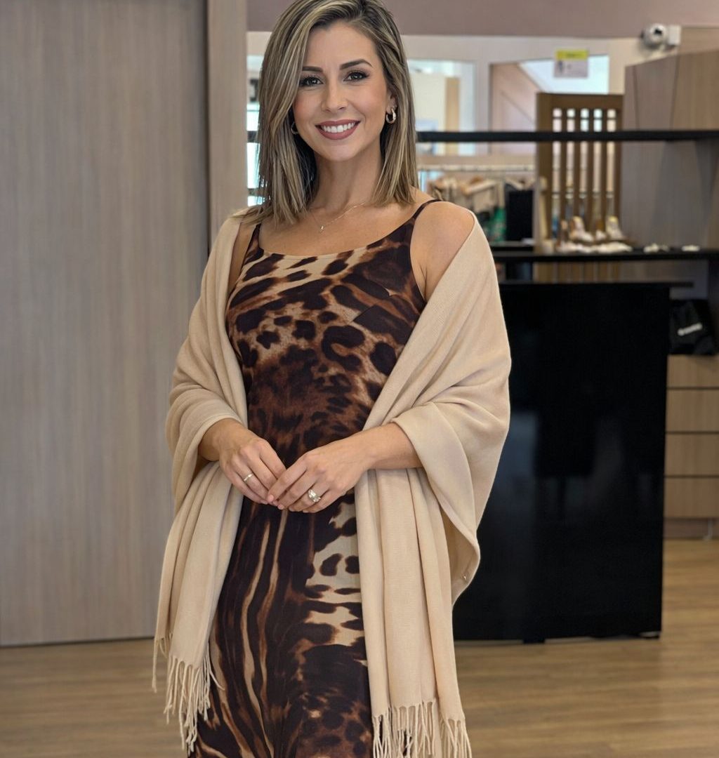 Modelo usando pashmina feminina com franjas sobre vestido estampado marrom, em ambiente interno de loja, compondo um look elegante e sofisticado.