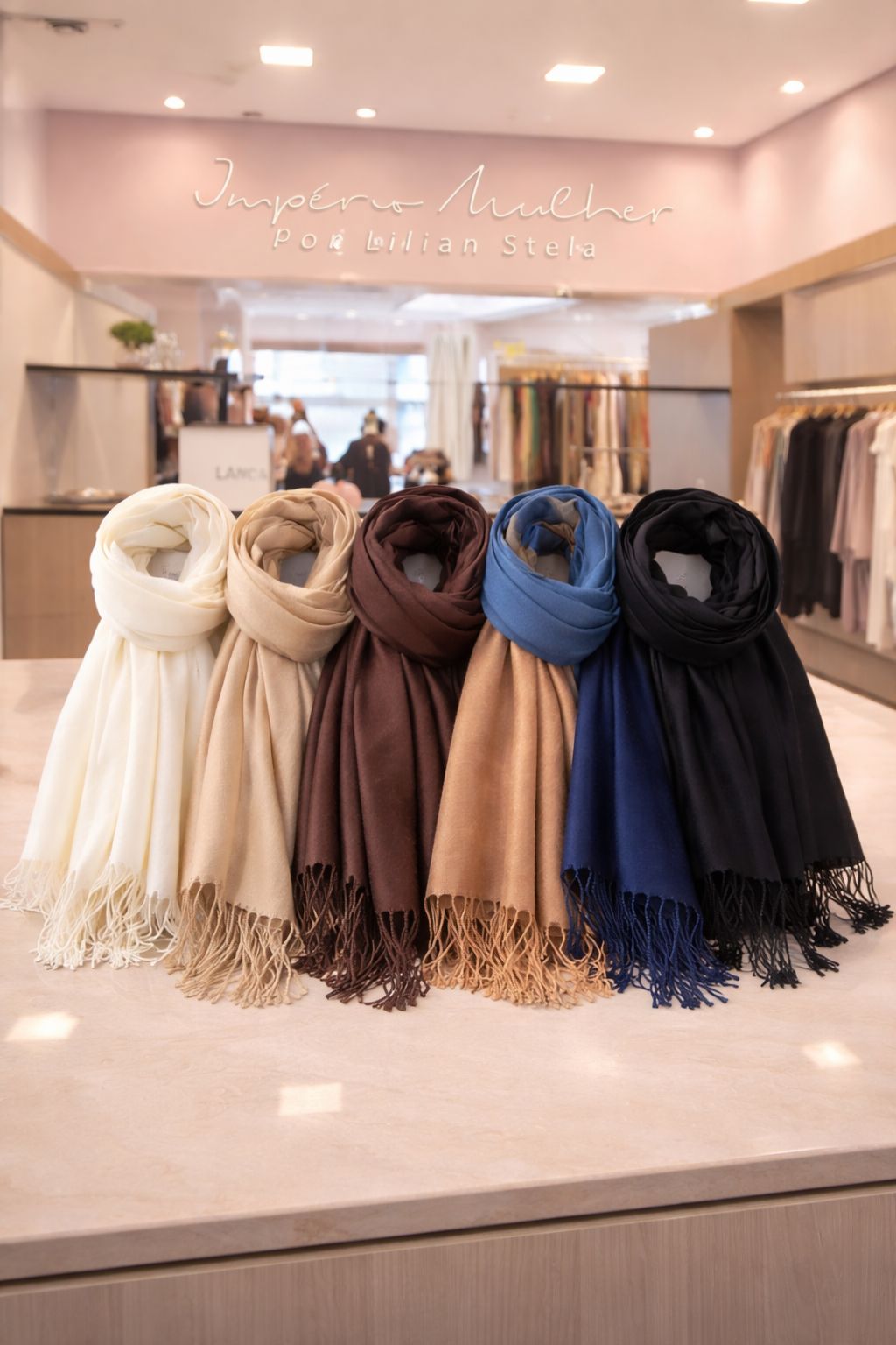 Modelo usando pashmina feminina com franjas sobre vestido estampado marrom, em ambiente interno de loja, compondo um look elegante e sofisticado.