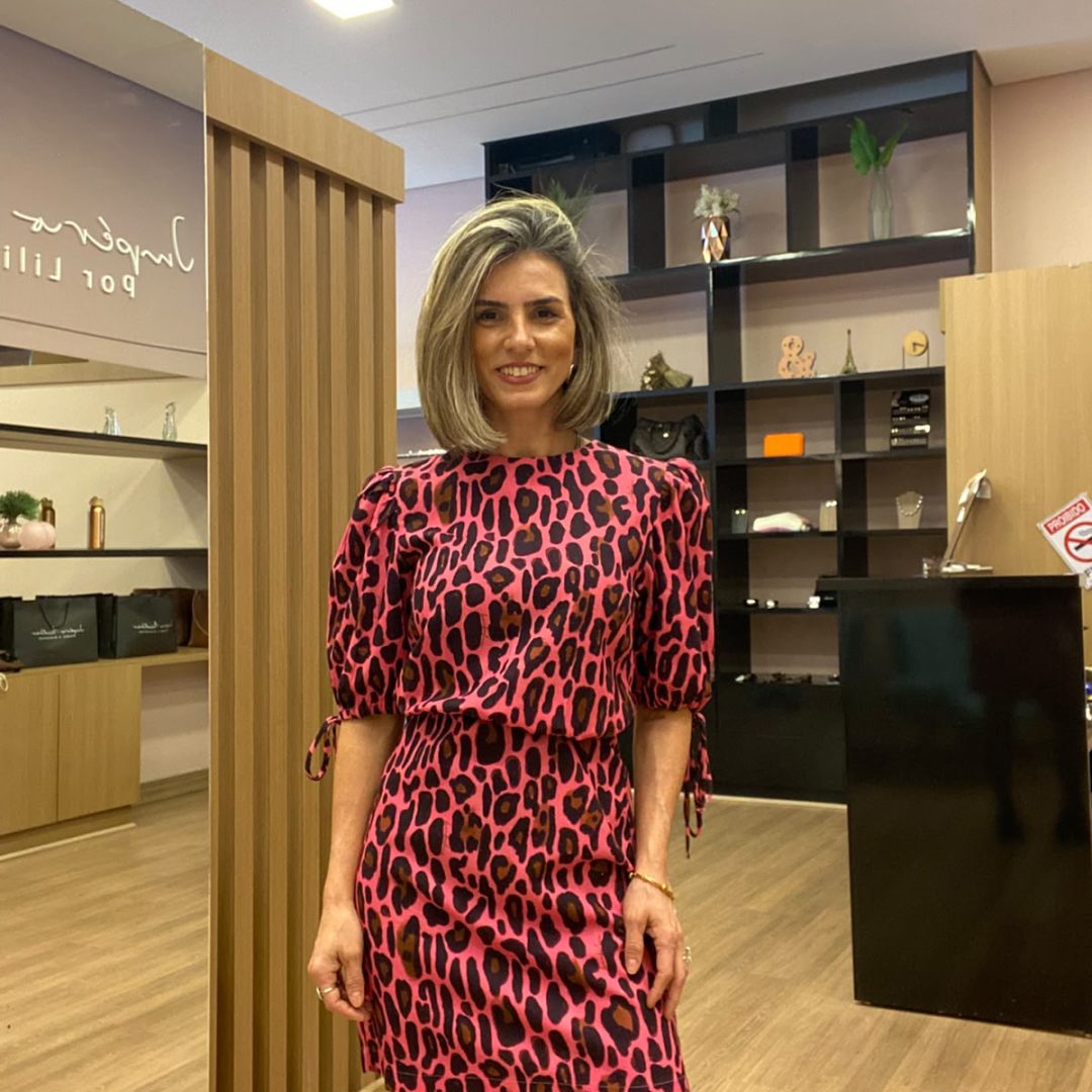 Modelo usando vestido curto animal print rosa e preto com mangas bufantes e cintura marcada, combinado com bota preta em loja de moda feminina.