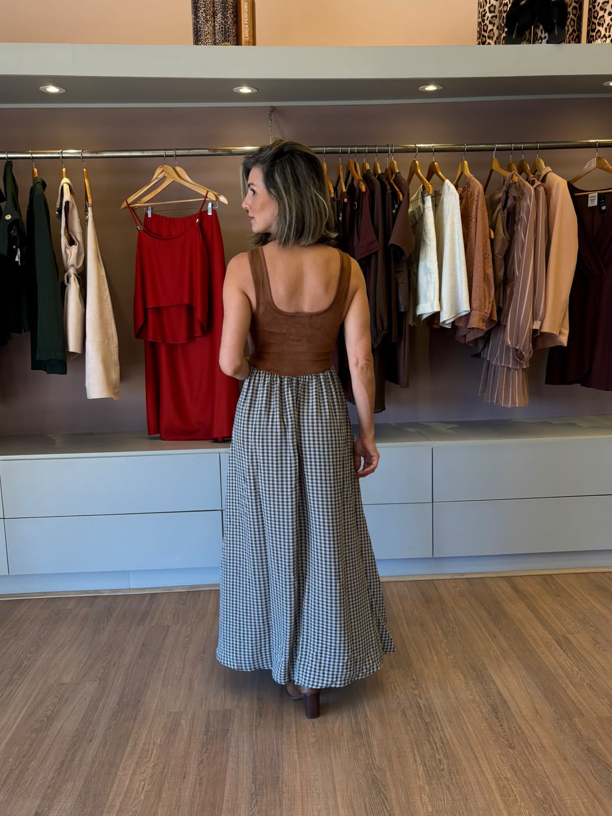 Modelo usando vestido midi com corpo em suede marrom, saia fluida xadrez e fenda frontal, em look elegante e sofisticado.
