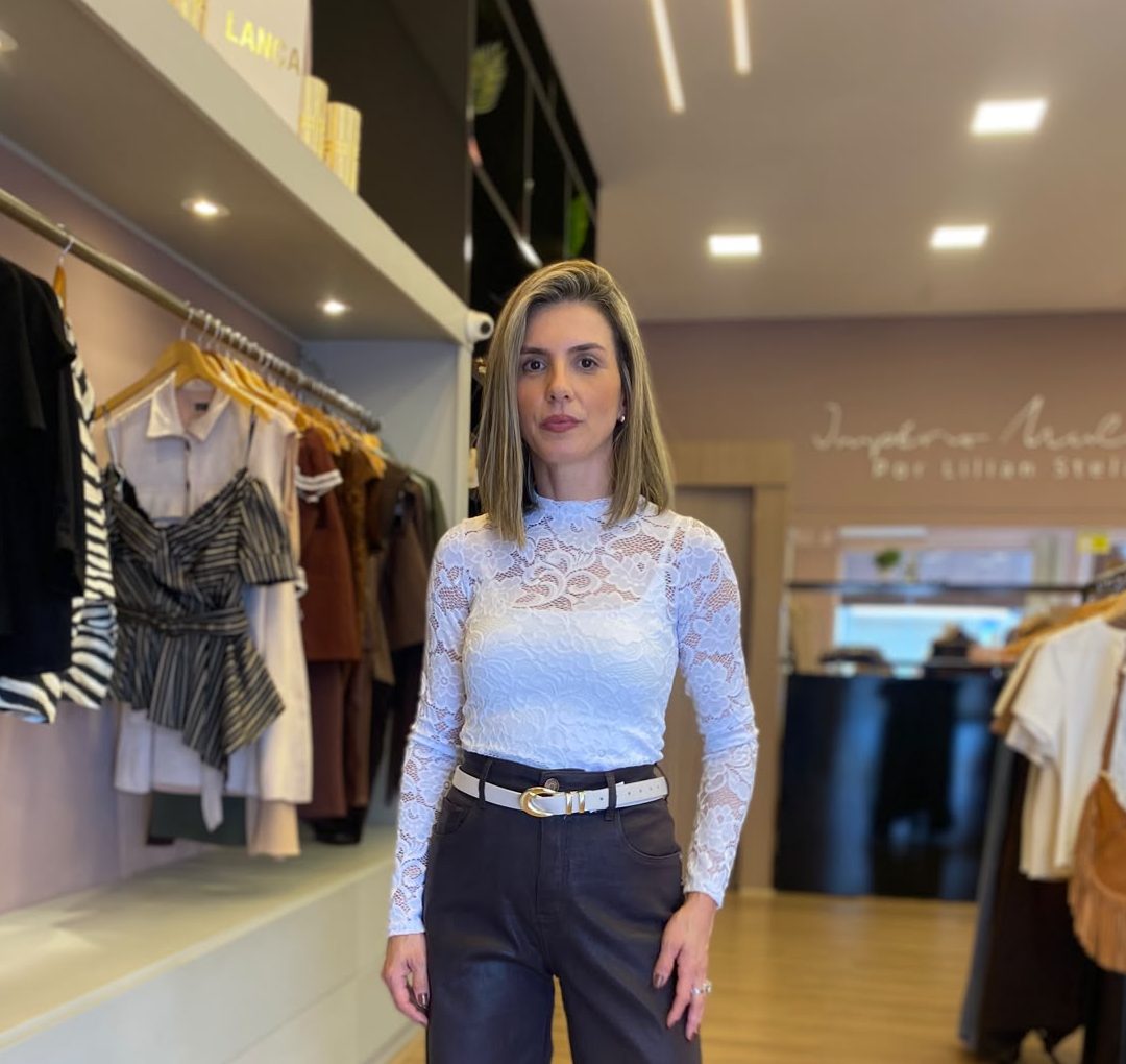 Modelo usando blusa feminina branca de renda com mangas longas e gola alta, ideal para composições elegantes e sofisticadas.