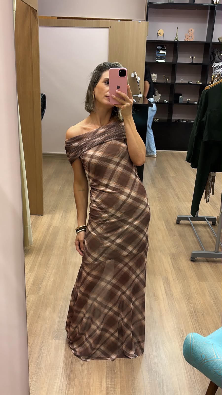 Modelo vestindo vestido longo xadrez marrom com decote ombro a ombro, modelagem elegante e caimento fluido, ideal para festas, eventos e ocasiões especiais.