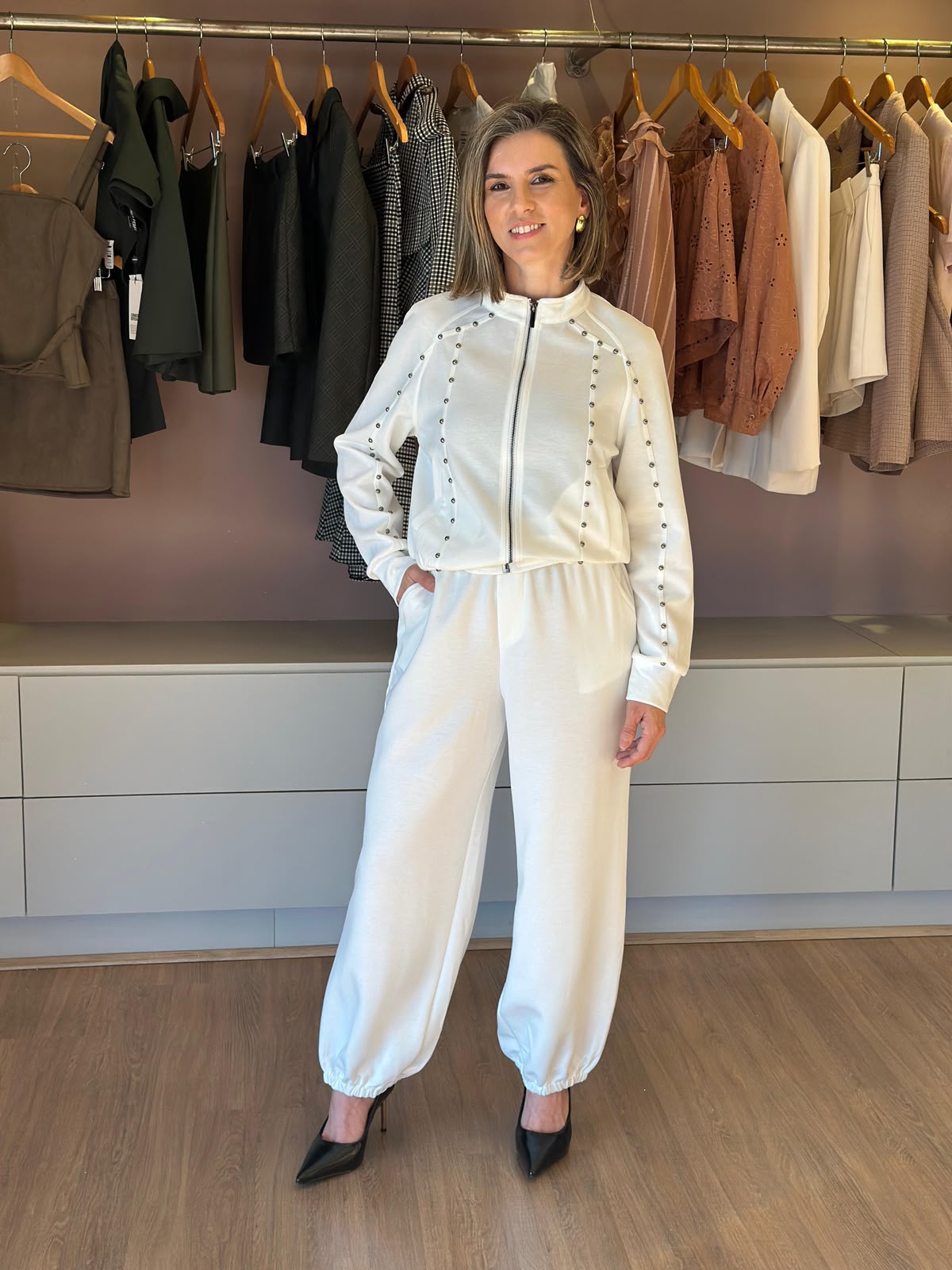 Modelo veste conjunto feminino off white com jaqueta de zíper e aplicações, calça jogger