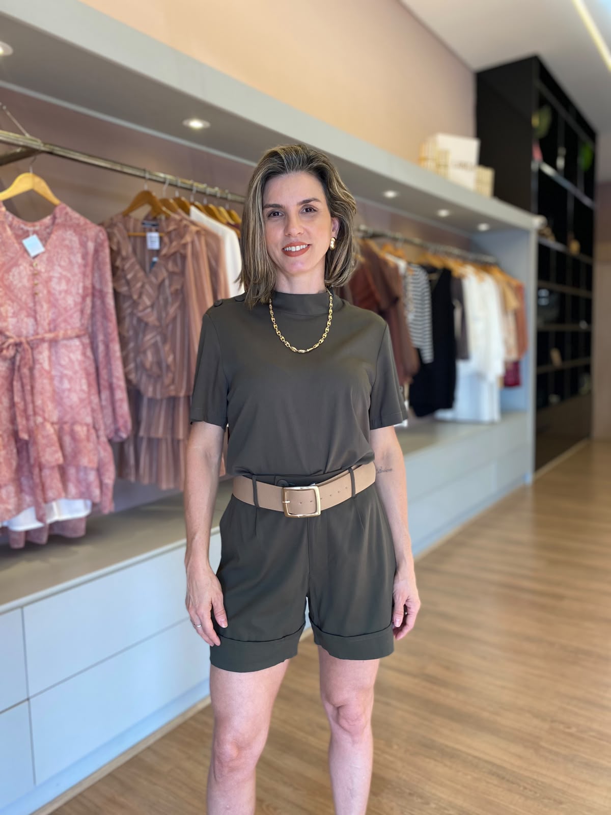 Modelo veste conjunto feminino verde militar com blusa de manga curta, short de alfaiataria com pregas e cinto largo bege.
