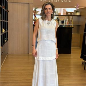 Modelo veste conjunto branco composto por blusa sem mangas e saia longa, em tecido leve e fluido.