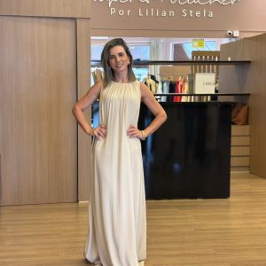 Vestido longo em tom claro, modelo fluido, sem mangas, com gola franzida e caimento elegante.
