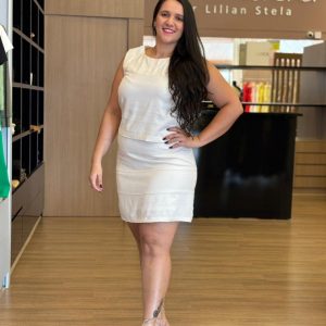 Modelo vestindo conjunto feminino off white com blusa de pregas e saia reta.