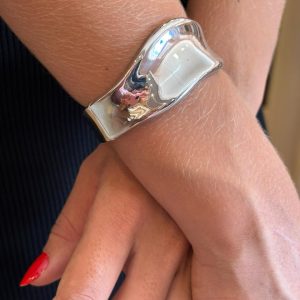 Bracelete feminino prateado largo moderno sendo usado no pulso em look elegante.