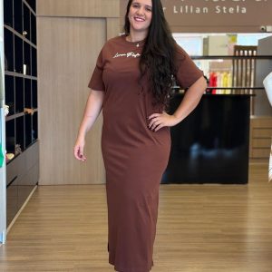 Modelo vestindo vestido super midi marrom de manga curta com modelagem reta e fenda lateral.