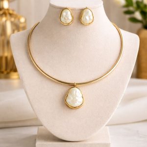 Conjunto feminino dourado com colar rígido e pingente de pérola orgânica acompanhado de brincos delicados, elegante e moderno.