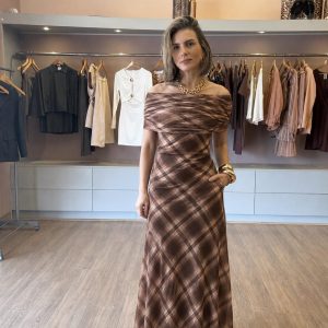 Modelo vestindo vestido longo xadrez marrom com decote ombro a ombro, modelagem elegante e caimento fluido, ideal para festas, eventos e ocasiões especiais.