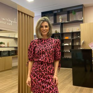 Modelo usando vestido curto animal print rosa e preto com mangas bufantes e cintura marcada, combinado com bota preta em loja de moda feminina.