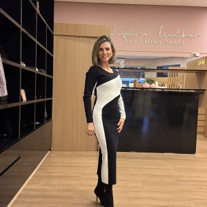 Modelo usando vestido midi preto e branco de manga longa com recortes geométricos que valorizam a silhueta, combinado com bota de salto preta.