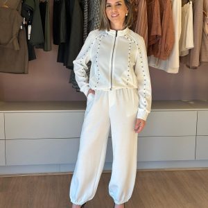 Modelo veste conjunto feminino off white com jaqueta de zíper e aplicações, calça jogger